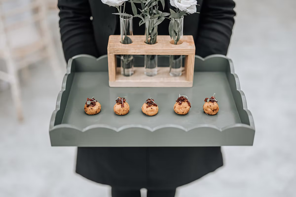 Canapés presented on a sage-green tray with white flowers in glass vases