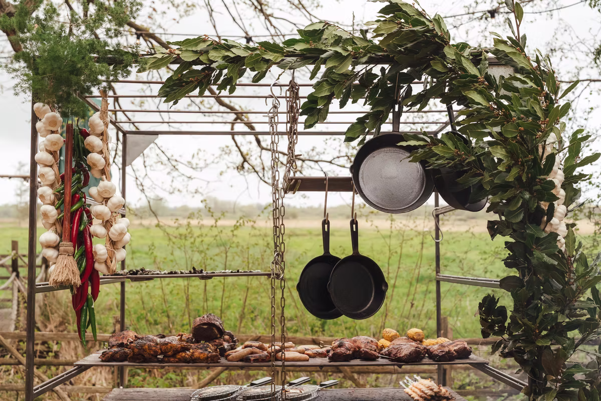 Asado grill dressed with foliage, with food cooking beneath hanging cast-iron pans